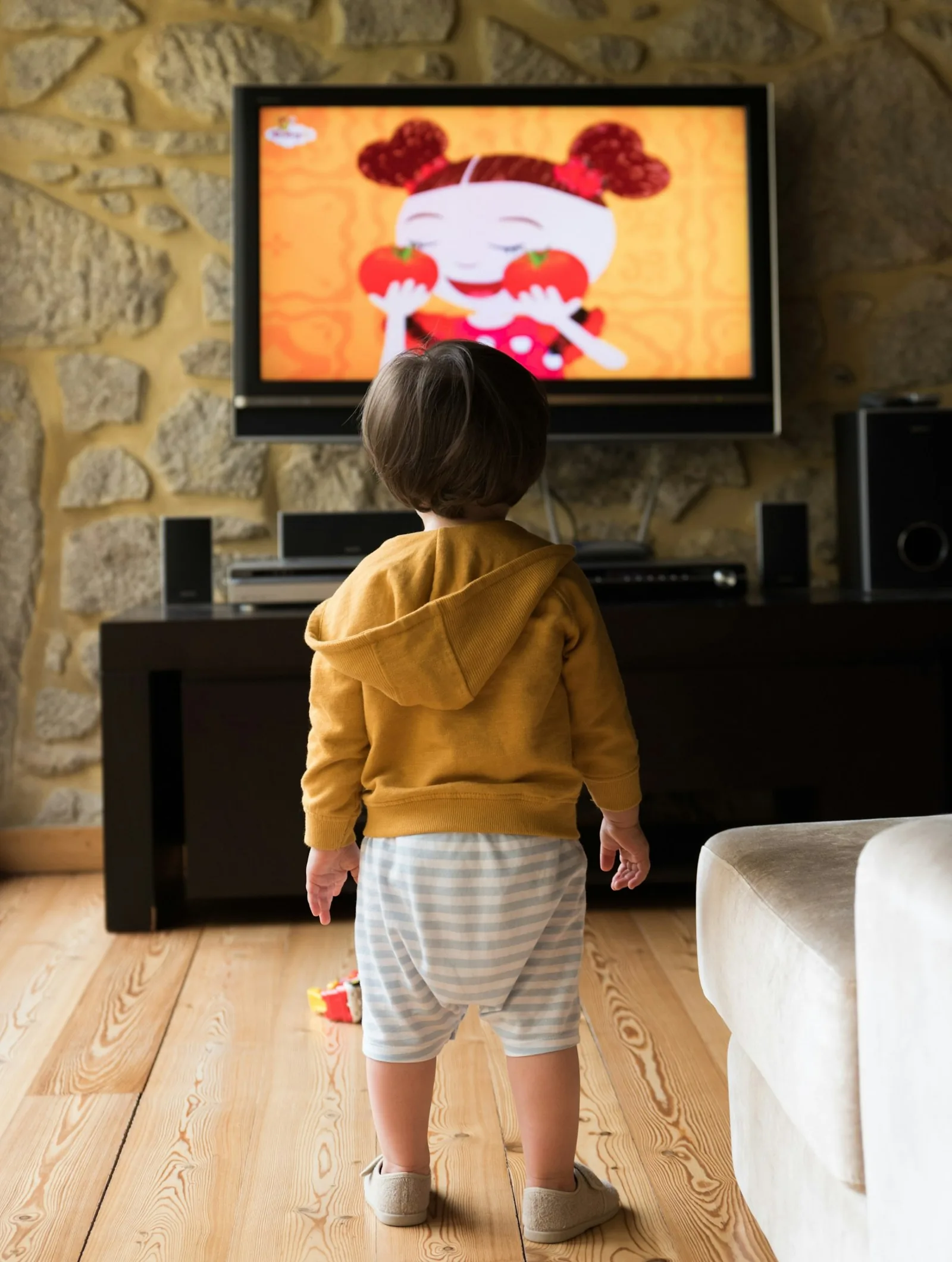 A young child standing in front of a television, watching from behind.